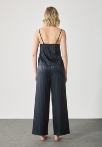 Pigiama in satin blu con design a righe, composto da un top senza maniche e pantaloni a gamba larga, che mette in risalto una texture liscia e lucida.