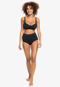 Set di bikini nero realizzato in tessuto a coste, con un top bralette dalle spalline larghe e uno slip a vita alta, che mette in mostra una texture liscia.