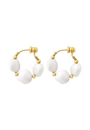 Boucles d’oreilles créoles en or avec trois perles blanches irrégulières chacune, avec une petite perle en or entre les perles sur fond blanc.