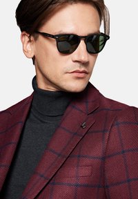 Czarne okulary przeciwsłoneczne z ciemnymi szkłami, noszone z szarym golfem i burgundową marynarką w kratę z niebieskimi akcentami i eleganckim wzornictwem.