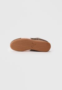 Brown rubber sole with a textured pattern, featuring a raised logo. Upper material shows contrasting colors with stitching details.
