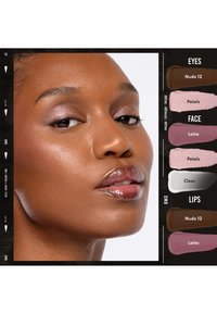 Ingrandimento di una donna con pelle liscia che indossa ombretto rosa shimmery, labbra lucide e un blush sottile, insieme a campioni di colore trucco etichettati.