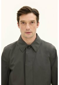 Mörkgrå kappa med stor krage och framknäppning. Slät textur med subtil lyster, lämplig för att bära över olika outfits.