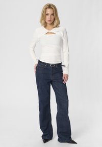 Vit ribbad långärmad topp med en framklippning, kombinerad med mörkblå utsvängda jeans. Jeansen har en silverfärgad spänne.
