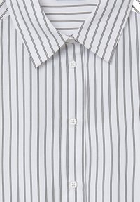 Chemise blanche à boutons avec des rayures verticales noires et un col pointu, montrant trois boutons blancs ronds sur le devant.