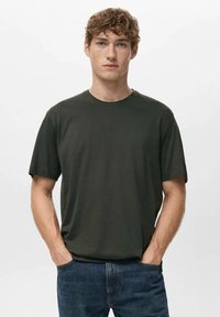 Ciemnozielona bawełniana koszulka z krótkim rękawem, z okrągłym dekoltem i luźnym krojem, zestawiona z niebieskimi dżinsami. Prosty, jednolity kolor bez wzorów.