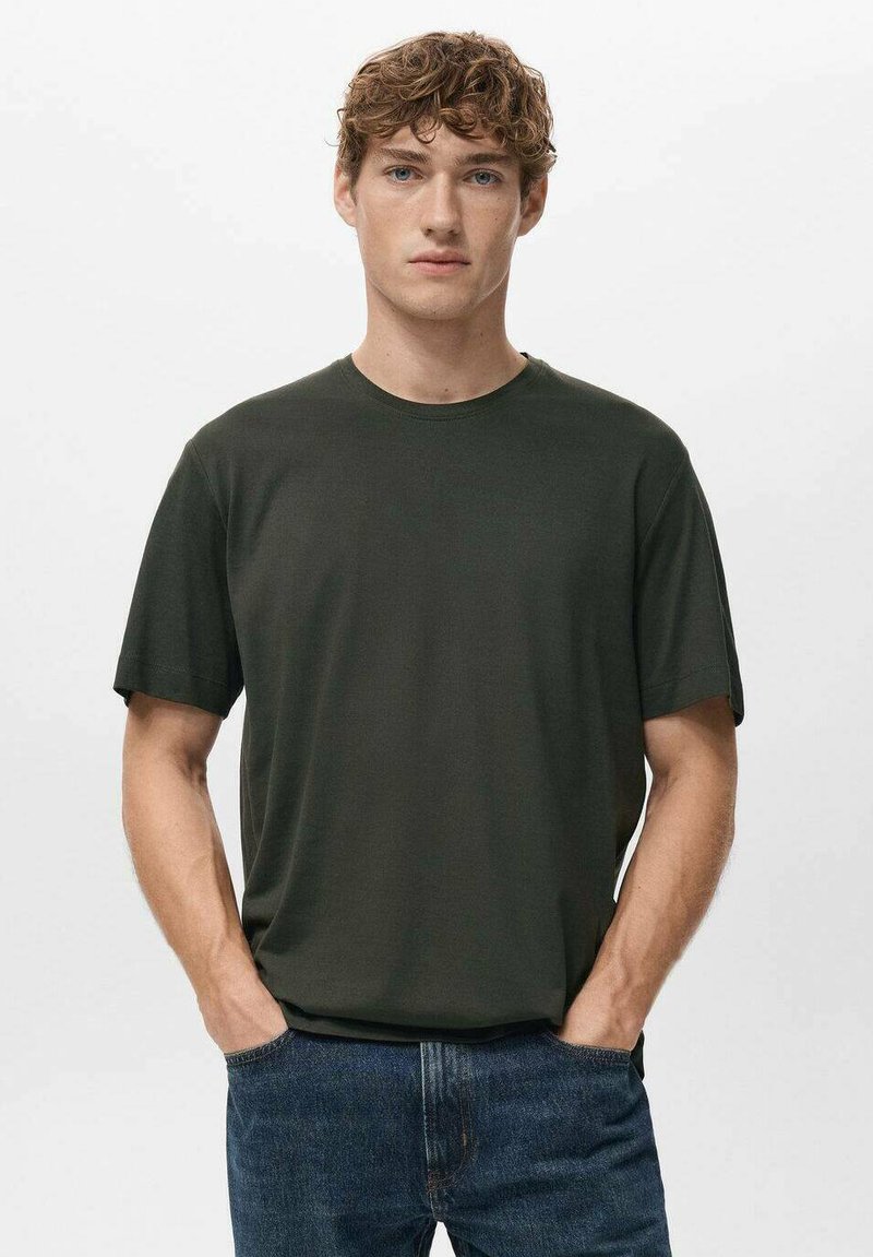 Ciemnozielona bawełniana koszulka z krótkim rękawem, z okrągłym dekoltem i luźnym krojem, zestawiona z niebieskimi dżinsami. Prosty, jednolity kolor bez wzorów.