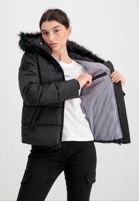 Czarna kurtka puchowa z kapturem wykończonym futrem, zapinana na zamek z przodu i z wewnętrzną kieszenią. Gładka tekstura z kontrastową szarością podszewki.