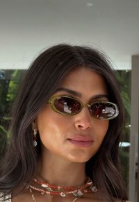 Žalios atspalvio, ovalo formos akiniai nuo saulės su rudu lęšiais. Lengvi plastikiniai rėmeliai su blizgiu paviršiumi. Sluoksniuotos, daugiakalbės kaklo grandinės.