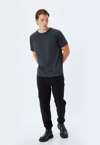 T-shirt corto grigio scuro a maniche corte con colletto rotondo e maniche raglan, abbinato a pantaloni neri slim-fit e stivali neri alla caviglia.
