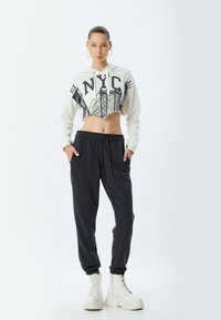 Forkortet hvid hoodie med sort NYC grafik, parret med mørke joggers. Modellen har hvide platformstøvler med kraftig sål på.
