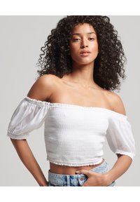 Hvid off-the-shoulder crop top med struktureret stof og pufærmer, parret med lyseblå denim shorts.
