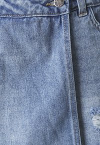 Světlá modrá džínová sukně s knoflíkovým zapínáním, poutky na opasek, se zabroušenou nášivkou a viditelnými stehmi. Měkká textilie s mírným vyblednutím.