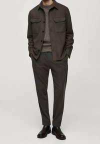 Oliivivihreä nappivyötärötakki, jossa on kaksi rintataskua, teksturoitu harmaa neule, kapenevat harmaat housut ja mustat nahkaiset nilkkasaappaat.