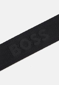 Juodas audinio diržas su iškilmingu "BOSS" logotipu, tekstūra paviršiumi ir plokščia konstrukcija. Tinka įvairiems aksesuarams ar drabužiams.