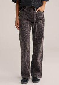 Pantalones de pierna ancha en marrón oscuro con un estampado de leopardo. Hechos de tela suave, cuentan con un cordón en la parte delantera y cinco bolsillos. Combinados con zapatos negros.