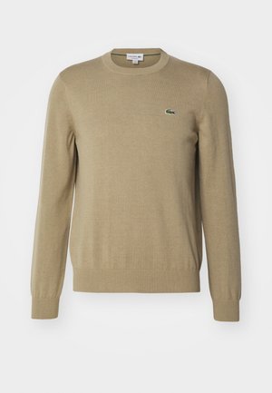 Maglione lavorato a maglia beige con scollo tondo, polsini e orlo a costine, con un piccolo logo di un coccodrillo verde sul lato sinistro del petto.