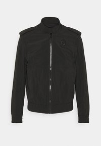 Černá bomber bunda vyrobená z lehkého materiálu, s vysokým límcem, zipovým zapínáním, ramenními epauletami a vyšívaným logem na hrudi.