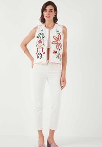 Geborduurde vest met kleurrijke bloemenpatronen op een witte achtergrond, met een cropped ontwerp en een ronde halslijn. Witte broek complementeert de look.