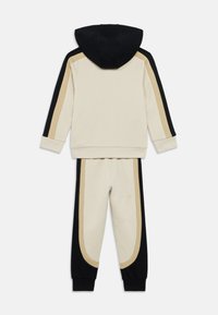 Σετ φούτερ με κουκούλα και παντελόνι, με κρεμ βάση και μαύρες και μπεζ ρίγες στα πλάγια. Μαλακή υφή, casual σχεδιασμός.