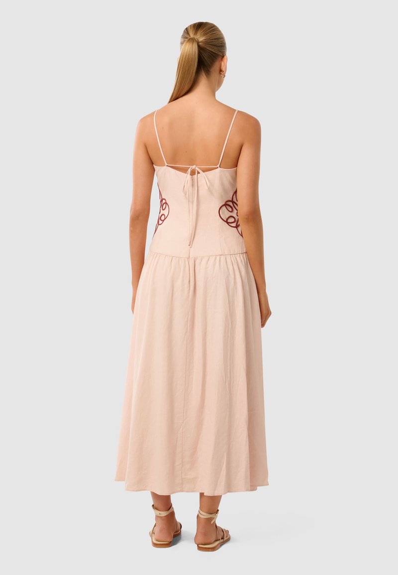 Maxi-jurk van zacht roze stof, met een aansluitend lijfje met rode borduursels en verstelbare spaghettibandjes, die uitloopt in een volle rok.