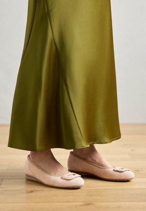 Bailarinas de color rosa claro con parte superior de tela suave, que presentan un detalle floral y una suela baja y texturizada, combinadas con un vestido verde oliva.