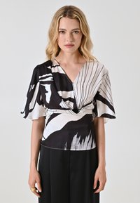 Blusa bianca e nera con scollatura a V, caratterizzata da un mix di motivi astratti e righe, maniche corte a balza e vita aderente.
