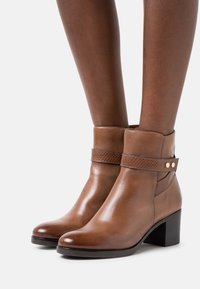 Bottes basses en cuir marron avec une finition lisse, une sangle texturée et un accent géométrique. Elles présentent une semelle à talons épais pour plus de stabilité.
