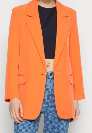 Heldere oranje blazer met een getailleerde pasvorm, met sja lapels, enkele knoopsluiting en zijzakken. Draagt over een zwart cropped top met gestreepte jeans.