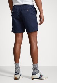 Marinblå bomullsshorts med elastisk midja, två bakfickor och uppvikta fållar, kombinerat med vita sneakers och grå strumpor.