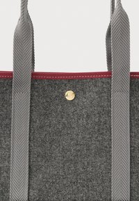 Γκρίζα τσάντα tote από ύφασμα με δύο γκρίζες πλεχτές λαβές, μαρουνί περιθώριο στην κορυφή και μια μικρή χρυσή κουμπωτή κλείσιμο στο κέντρο.