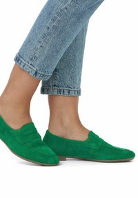 Mocassins en suède vert avec une semelle plate, dotés d'un design simple et d'une sangle décorative à l'avant. Associés à un jean en denim clair retroussé.