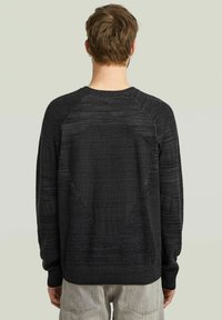 Pull en maille noir avec un design texturé, des manches raglan et des bords-côtes. Le dos présente des motifs détaillés avec différentes techniques de tricot.