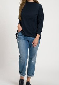 Marineblauwe longsleeve top met een ronde hals en diagonale stikdetails, gecombineerd met lichtblauwe distressed jeans en marineblauwe veterschoenen.