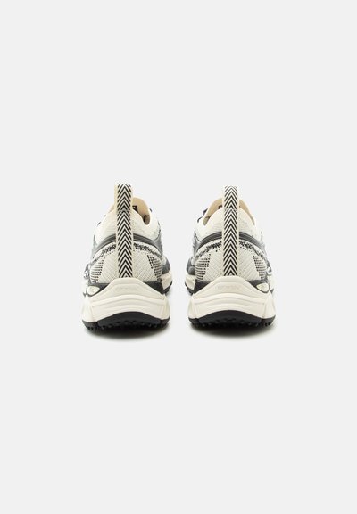 Ζευγάρι αθλητικών παπουτσιών σε λευκό και μαύρο με μοτίβο, εμφανιζόμενα από πίσω, με παχιά σόλα και κάθετες ταινίες για κράτημα.