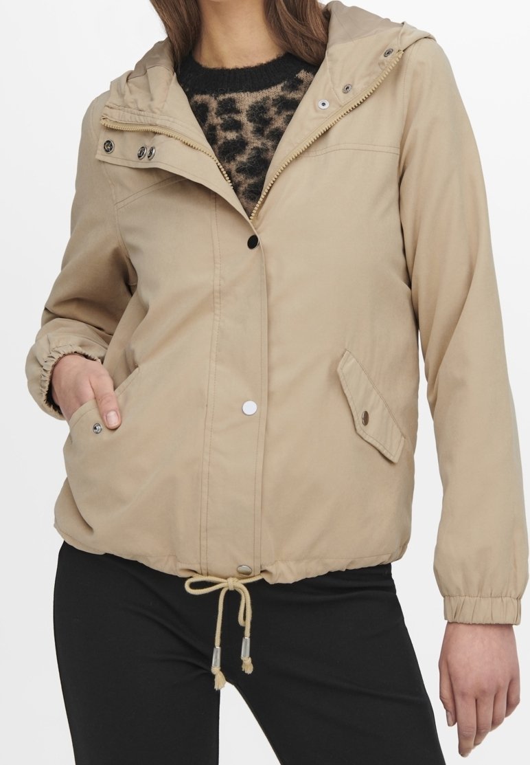 Beige hooded jacket with buttons and zipper, elastic cuffs, drawstring waist, worn over leopard print sweater and black pants.