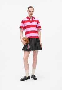 Rød og rosa stripete polo-skjorte med v-hals, kombinert med et svart plisséskjørt. Brun crossover-veske, knelange strømper og svarte loafers.