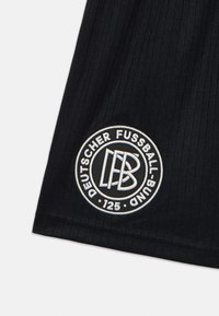 Svarta sportshorts med ribbad textur. Har en broderad cirkulär logotyp i vitt och kräm, med texten "Deutscher Fussball-Bund 125."