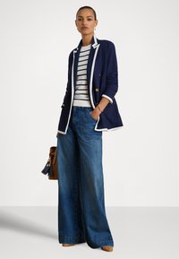 Marineblå dobbelspent blazer med hvit kant, stripete genser, vide jeans, brun håndveske og lyse brune vevde sko.