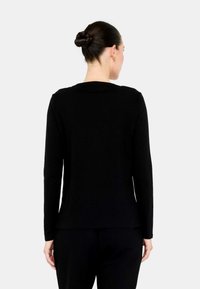 Top nero a maniche lunghe, design aderente, texture a coste, scollatura rotonda, con una leggera curva all'orlo. Vista posteriore che mostra dettagli minimi.