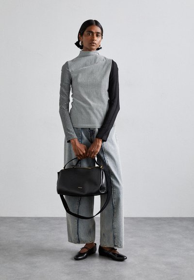 Haut à col roulé à motifs noir et blanc, jean en denim gris ample, sac à main en cuir noir avec quincaillerie dorée, et chaussures plates noires.