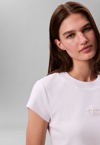Valge soonikkoes puuvillane T-särk lühikeste varrukatega, millel on vasakul rinnal väike reljeefne "Calvin Klein" logo.