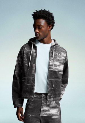 Hooded denim jacket featuring a black and white paint splatter pattern, paired with a light blue crew neck t-shirt and matching pants.