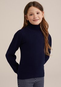 Jūras spēku ribota augsta apkakle ar garām piedurknēm; gluda tekstūra un pieguļošs dizains. Apvienots ar rakstainām biksēm, kas rotātas ar dimantiem.