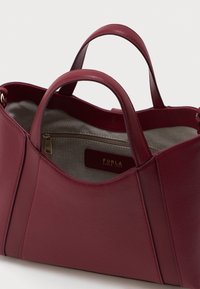 Burgundska kožna torba s dvostrukim drškama, s bež unutrašnjim oblogom i unutarnjim zip džepom označenim "Furla Since 1927" u zlatnom slovu.