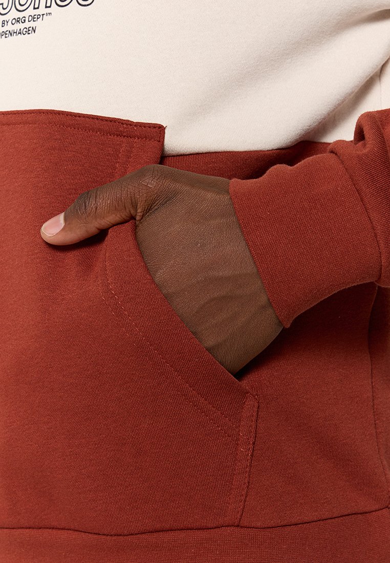 Sweat-shirt à manches longues présentant une partie supérieure crème et une partie inférieure de couleur rouille, fabriqué en tissu doux avec une poche kangourou.