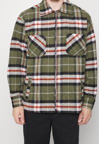 Zielona kurtka w kratę, wykonana z mieszanki wełny, z czerwonymi i czarnymi akcentami, z dwoma przednimi kieszeniami z klapami oraz zamek błyskawiczny.