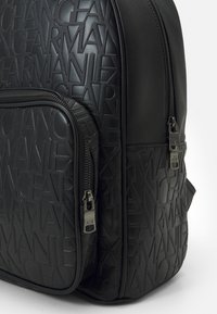 Zaino nero realizzato in materiale sintetico testurizzato, con un design del logo in rilievo, doppie cerniere e una tasca frontale.