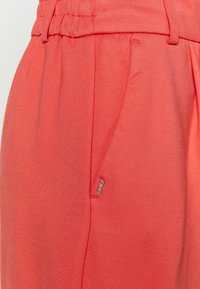 Pantaloni donna corallo dalla vestibilità ampia, con vita elastica, tasche laterali e un dettaglio con etichetta metallica del marchio. Tessuto morbido.