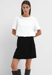 T-shirt bianco a maniche corte abbinato a una gonna nera avvolgente. L'outfit presenta un design minimalistico e una trama di tessuto liscia.